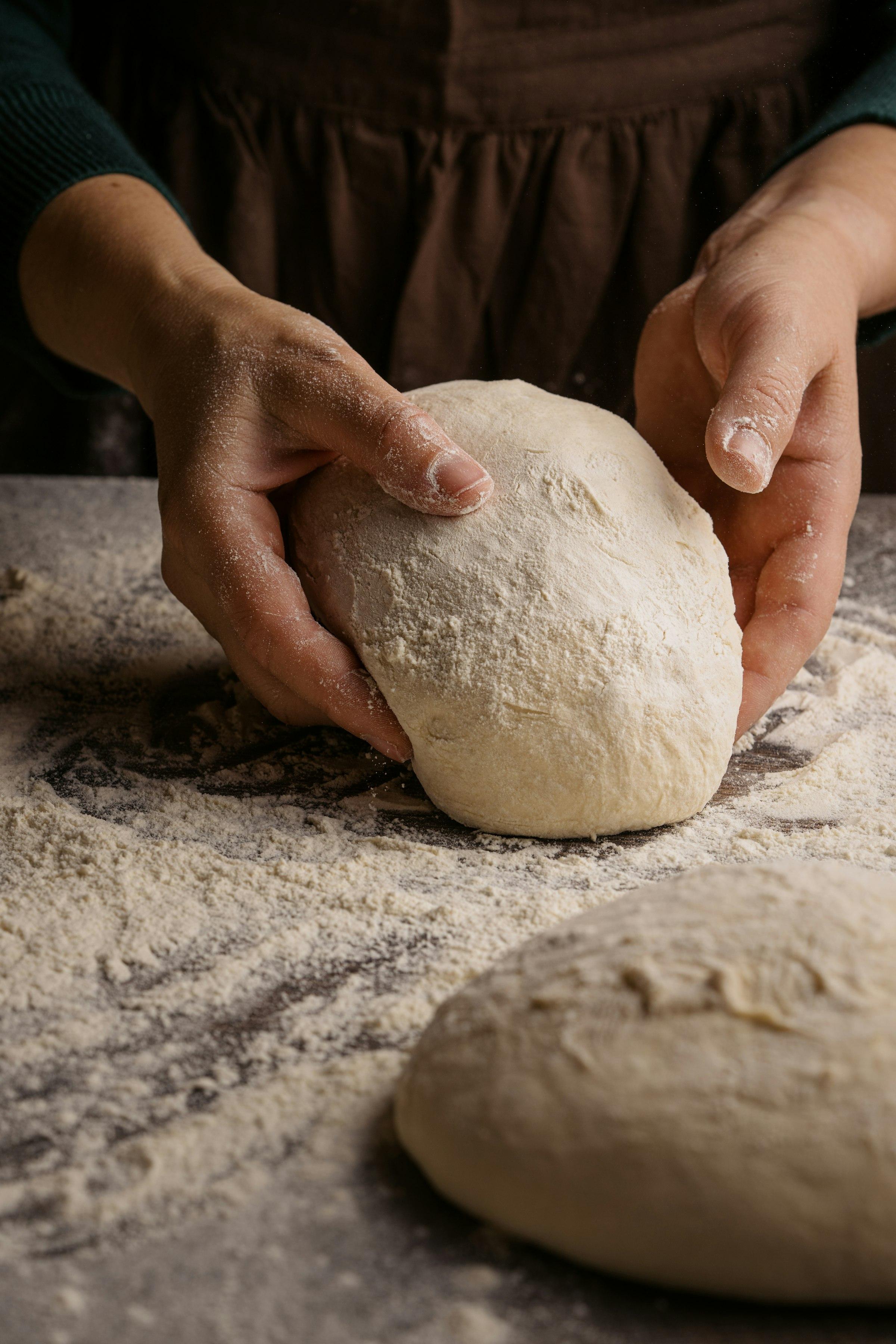 Hands kneading a ball of bread dough on a floured surface