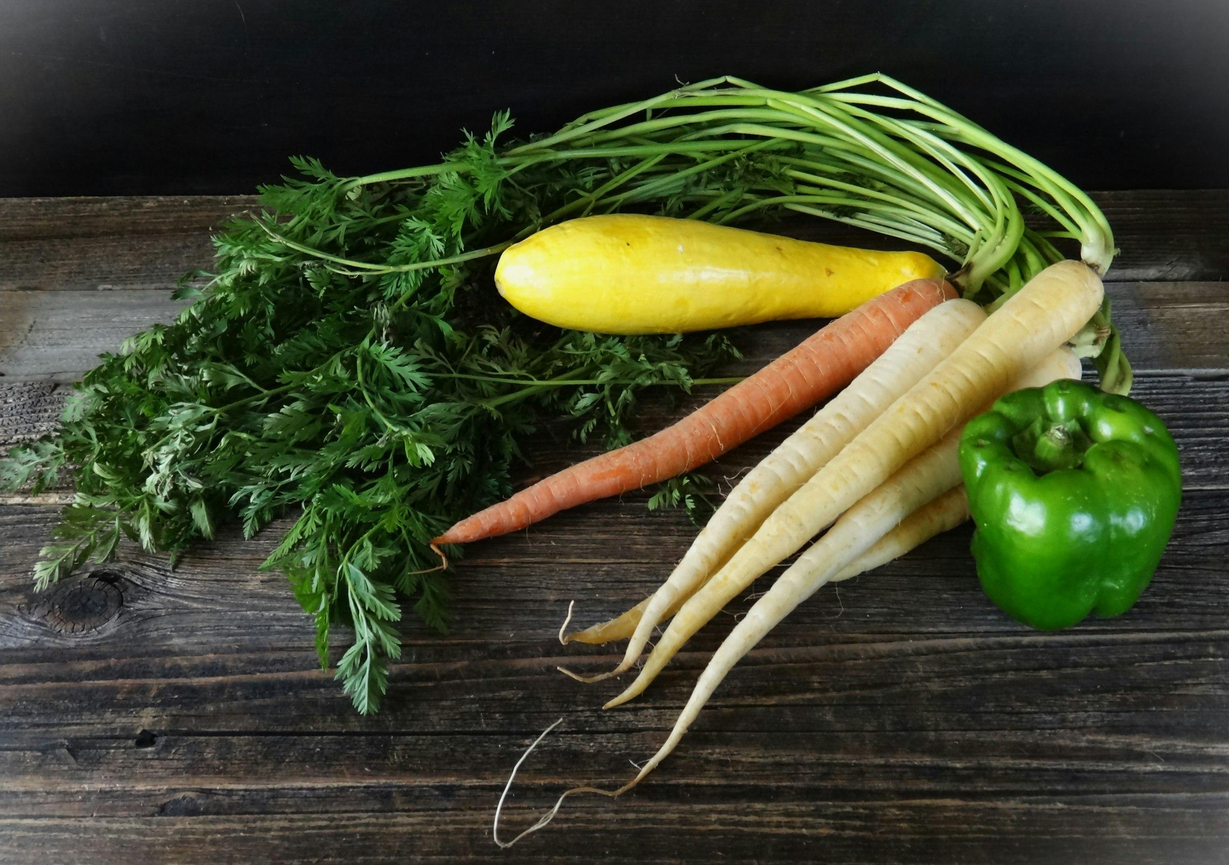 Fresh carrots, parsnips, squash, and a bell pepper on a dark wooden table