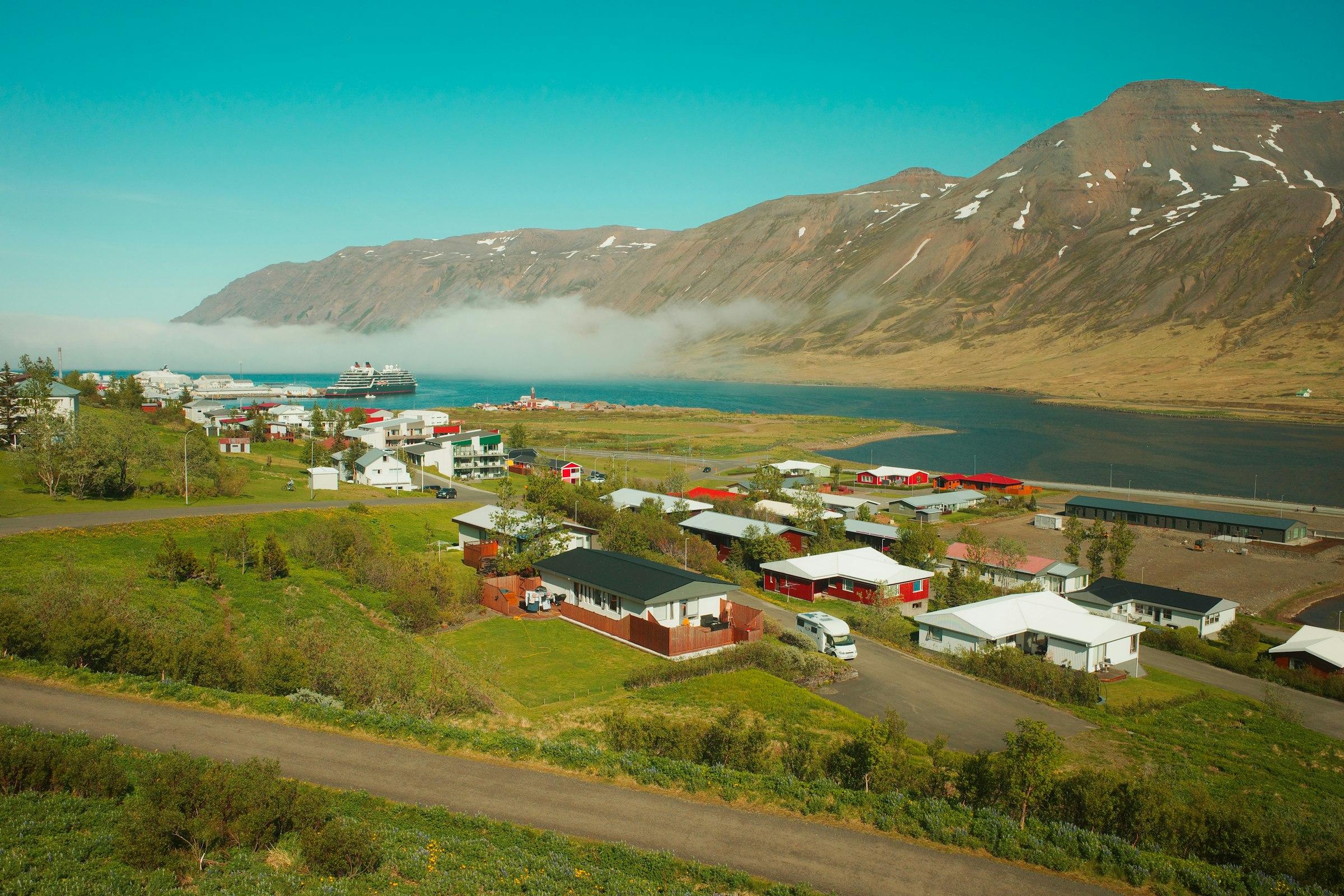 A small fjord-side coastal village with green hills and colorful houses